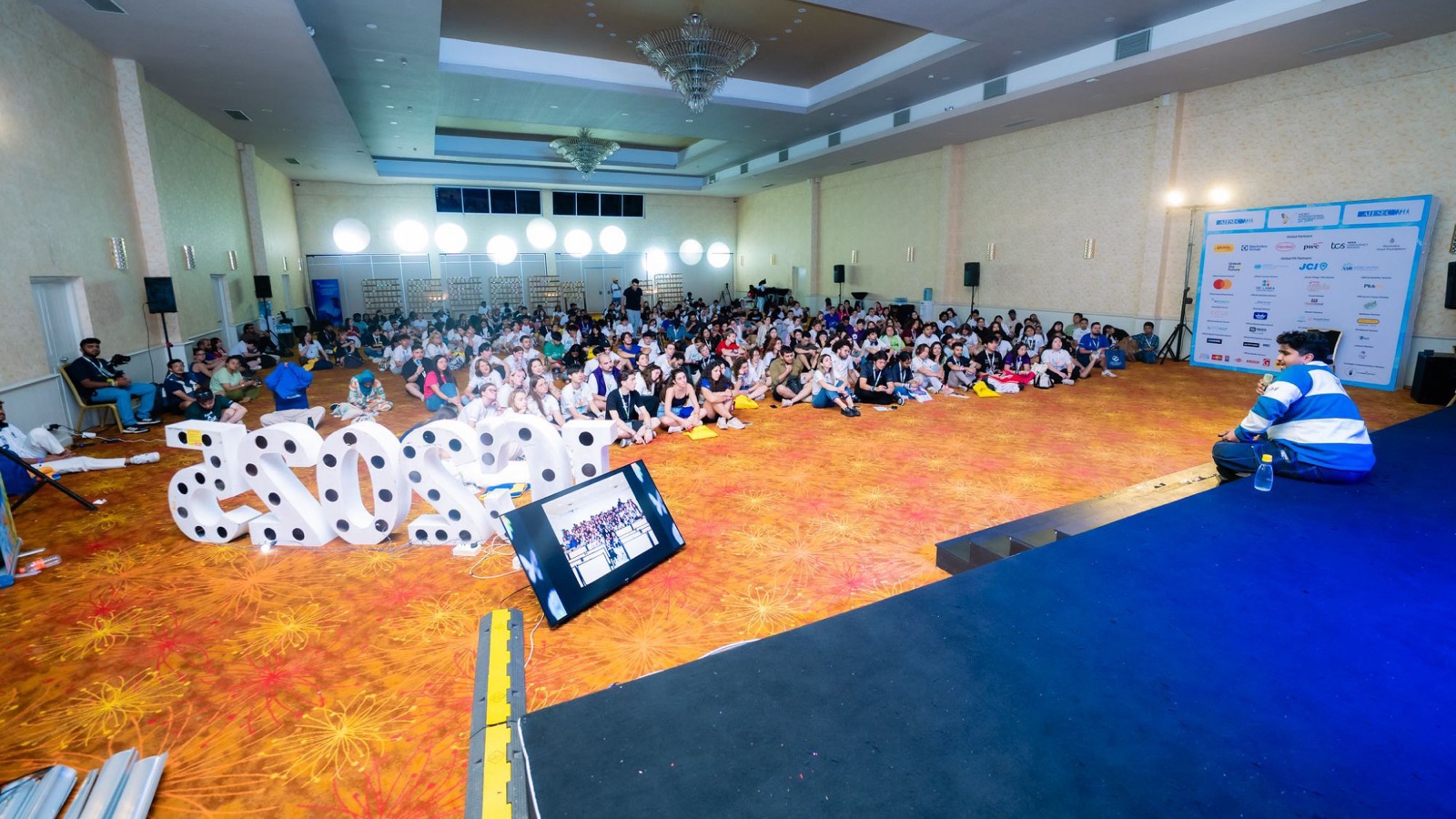 Arfan on stage speaking to a hall of several hundred people